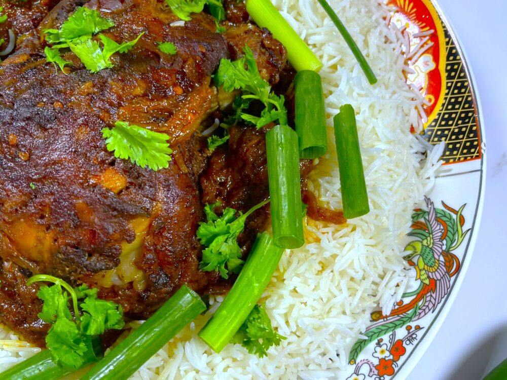 lamsbout uit de oven geserveerd met Afghaanse witte rijst, gegarneerd met verse koriander en lente-ui.