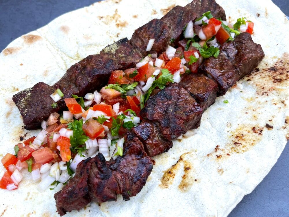 Tikka Kebab Spies geserveerd op lavash brood met een frisse salade van tomaat, ui en koriander